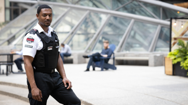 male security guard standing watch in the atrim of a college campus.