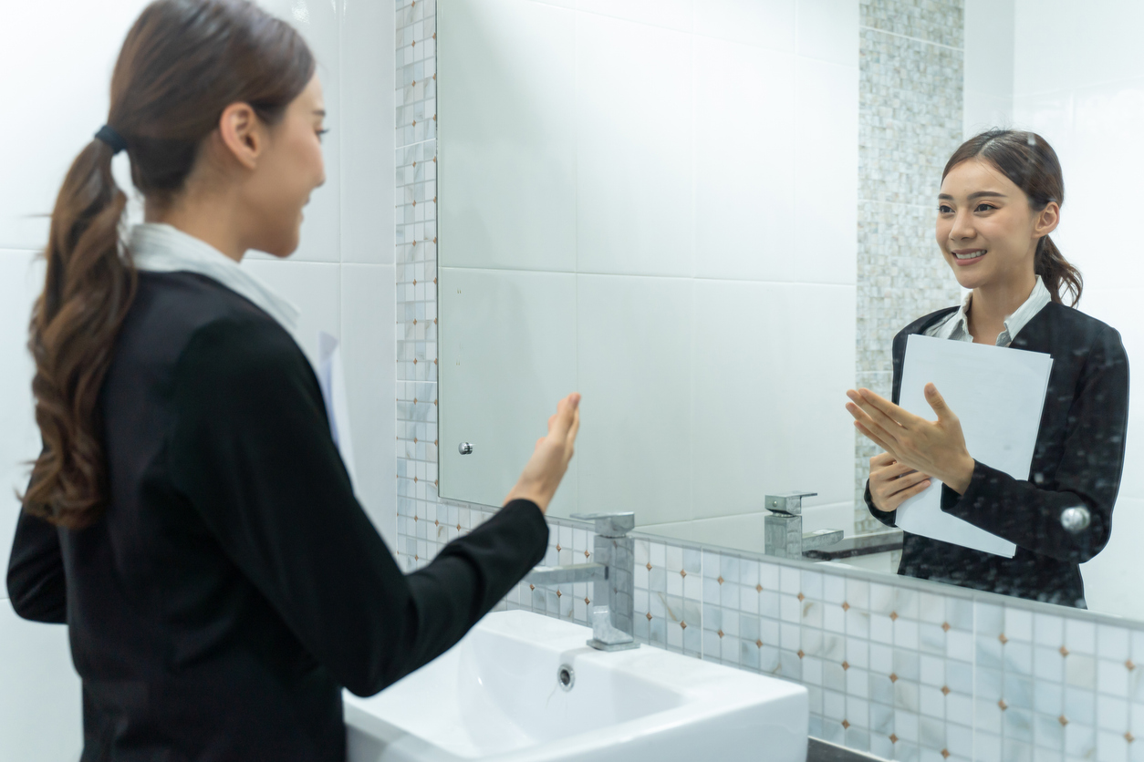 Asian applicant prepare for job interview in front of mirror at home. Attractive beautiful female feel nervous and excited while waiting for apply job with hr manager and practice speak with resume.